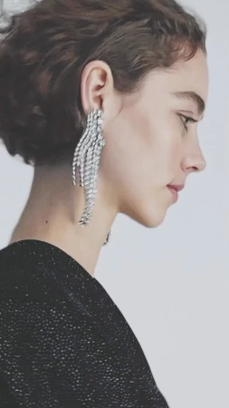 Profile portrait of a woman wearing large crystal fringe earrings and a black textured top against a plain light background.