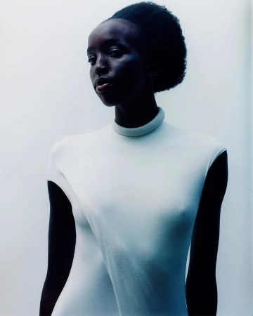Portrait of a Black woman in a white high-neck top against a bright white background by Charlie Gates