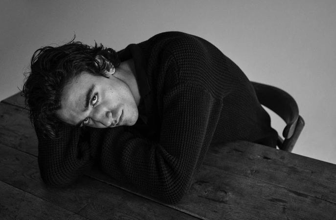 Monochrome portrait of a young man leaning his head on crossed arms at a wooden table in London by Charlie Gray