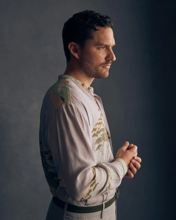 Profile portrait of a man wearing a patterned light grey shirt against a dark textured studio background by Charlie Gray