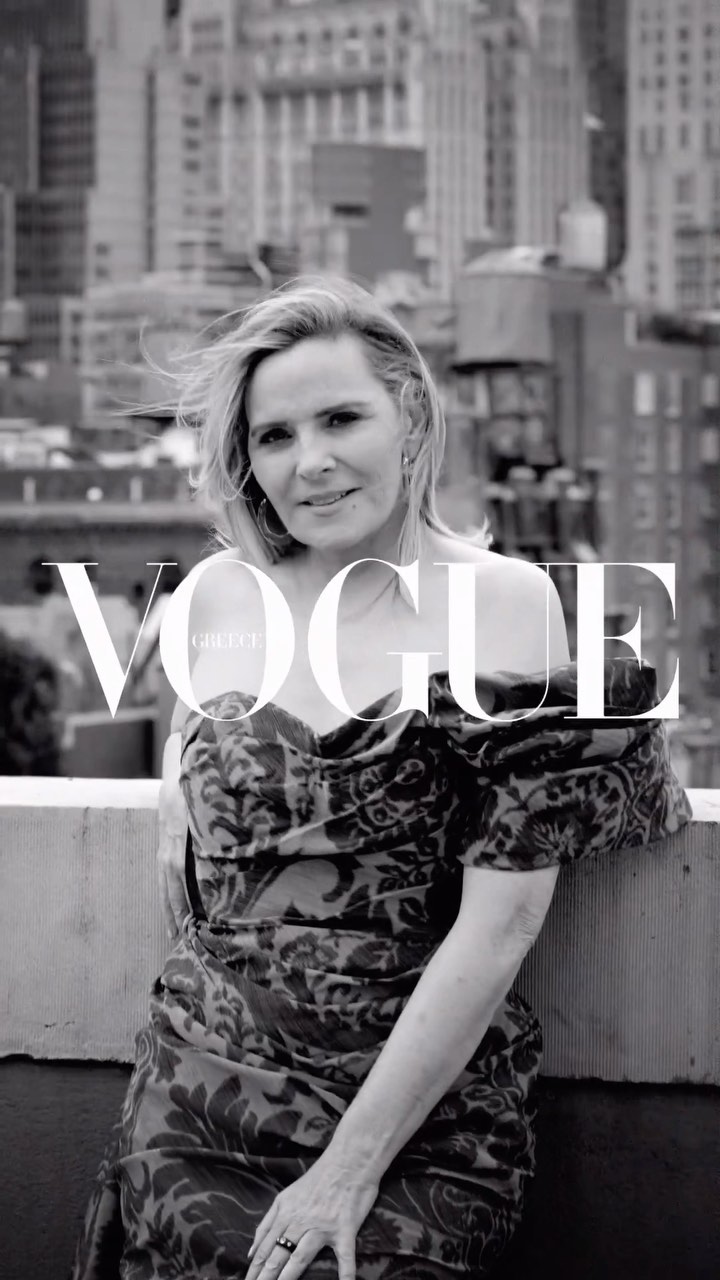 Monochrome portrait of Kim Cattrall leaning on a rooftop ledge against an urban backdrop with Vogue Greece text overlay