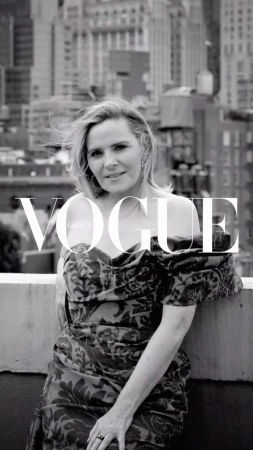 Monochrome portrait of Kim Cattrall leaning on a rooftop ledge against an urban backdrop with Vogue Greece text overlay