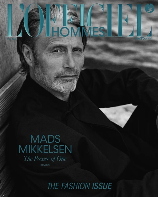 Magazine cover featuring Mads Mikkelsen in a close-up shot wearing a black jacket, against a textured background with the magazine title.