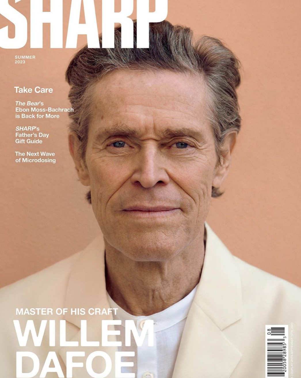 Willem Dafoe covers Sharp magazine; headshot of the actor wearing a light colored jacket, against a peach-colored background.