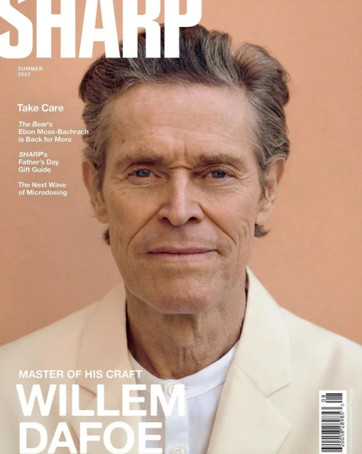 Willem Dafoe covers Sharp magazine; headshot of the actor wearing a light colored jacket, against a peach-colored background. 