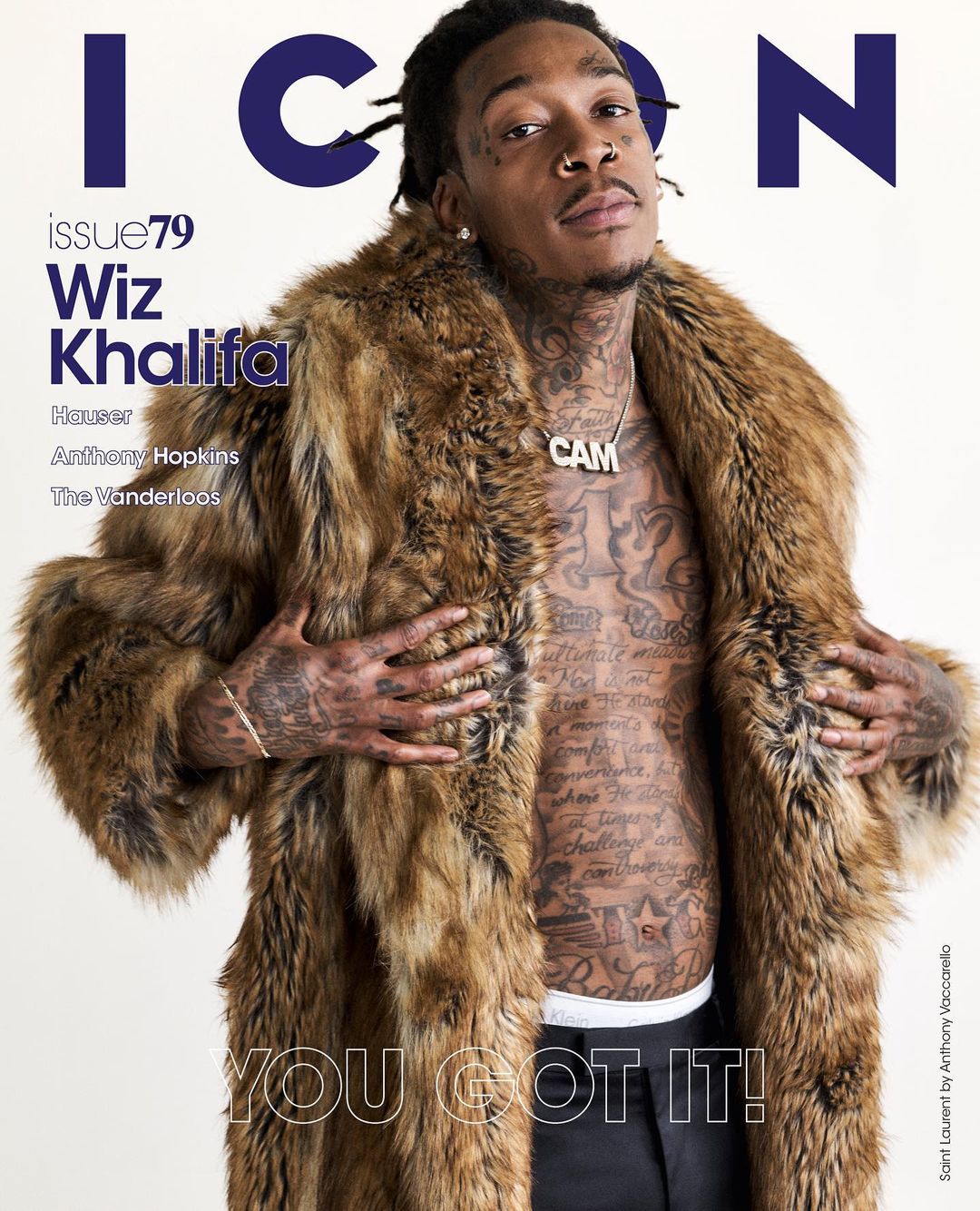 Wiz Khalifa, hip-hop artist, poses for a magazine cover wearing a fur coat and silver necklace. Tattoos are visible on his chest and arms.