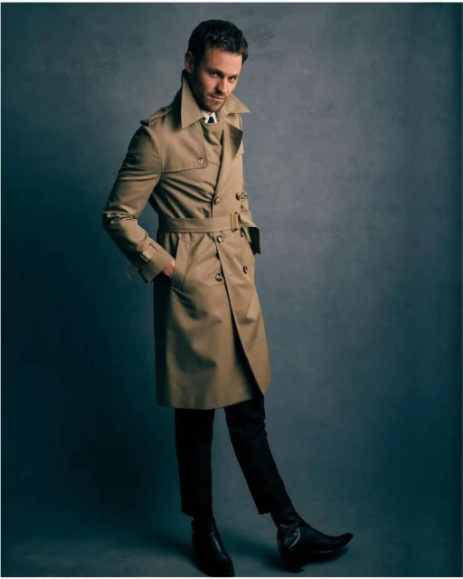 Full-length portrait of a man in a trench coat, posing against a gray background, showcasing fashion and style.