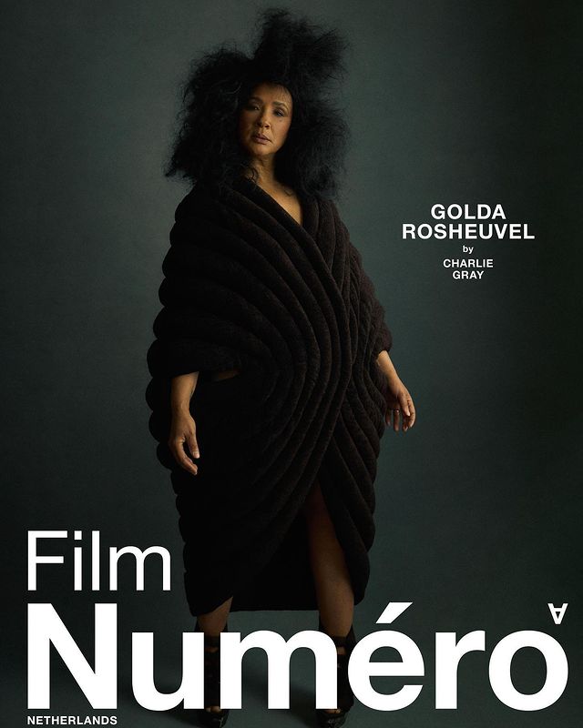 Fashion editorial shot featuring a woman in a black sculptural garment against a muted grey backdrop, promoting Film Numero Netherlands.