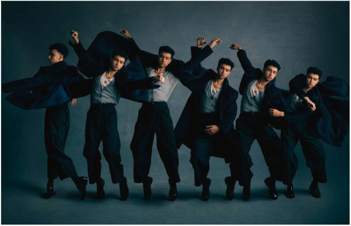 Multiple exposures of a young adult man in a gray vest, black trousers, and a dark coat in a dance-like pose against a gray background.