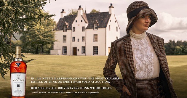 Woman in vintage attire poses outdoors alongside a Macallan whiskey bottle, set against a backdrop featuring a historic white building.