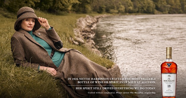 Woman in tweed suit and hat reclines in grassy field, next to water's edge, whisky bottle in the lower right corner, vintage fashion.