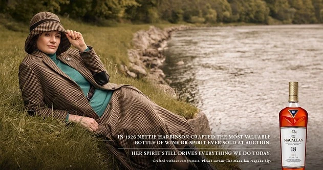 Woman in tweed suit and hat reclines in grassy field, next to water's edge, whisky bottle in the lower right corner, vintage fashion.