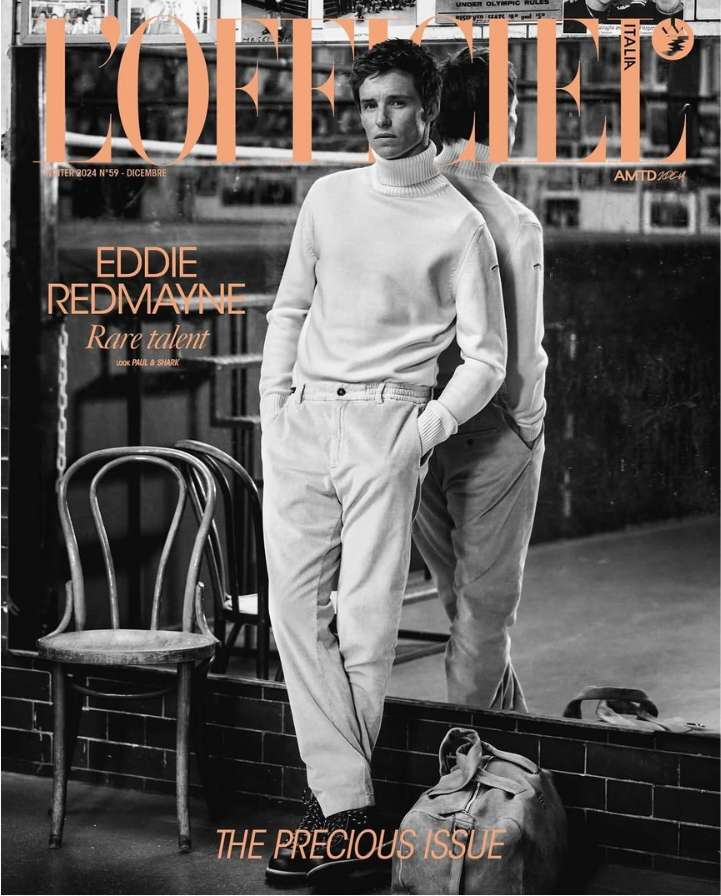 Magazine cover featuring Eddie Redmayne in a white turtleneck and cream pants, with a mirrored reflection and background details.