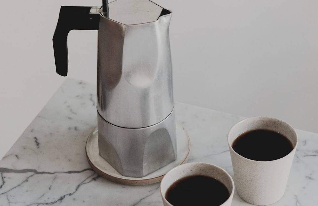 Moka pot and two cups of coffee arranged on a marble surface against a neutral backdrop, creating a minimalist coffee still life.