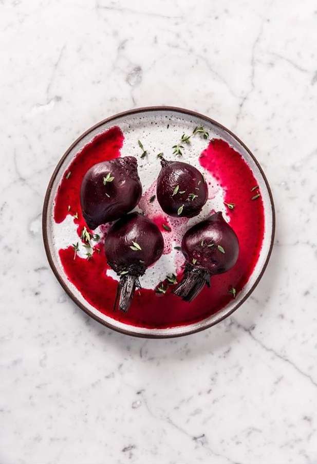 Overhead view of roasted beets on a speckled plate with red sauce and herbs against a marble background. Food photography.