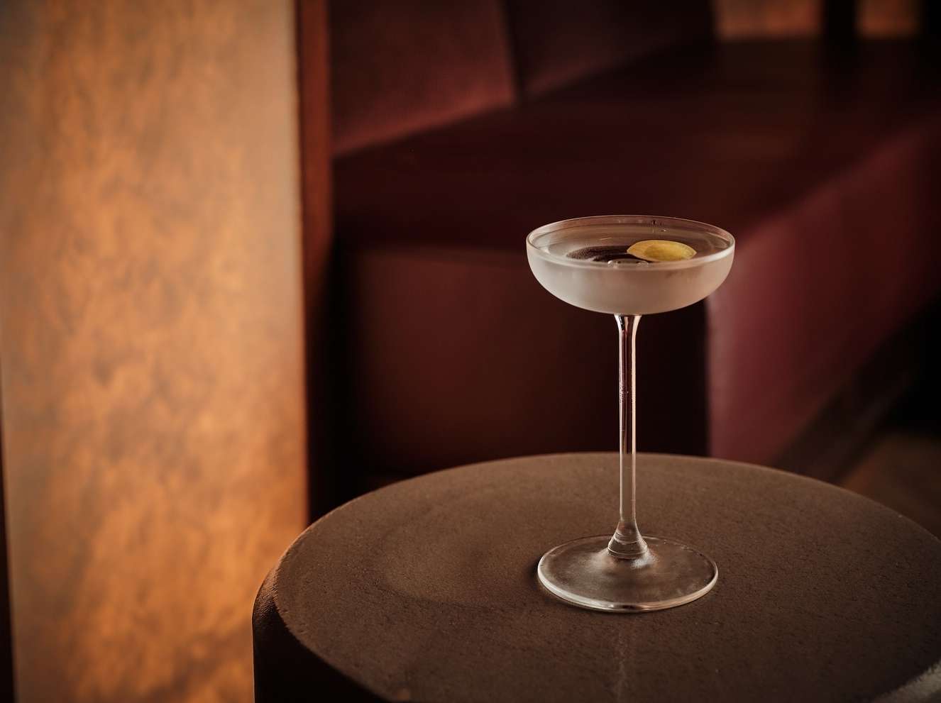 Elegant martini cocktail in coupe glass with citrus garnish on round table with textured background, creating a sophisticated ambiance.