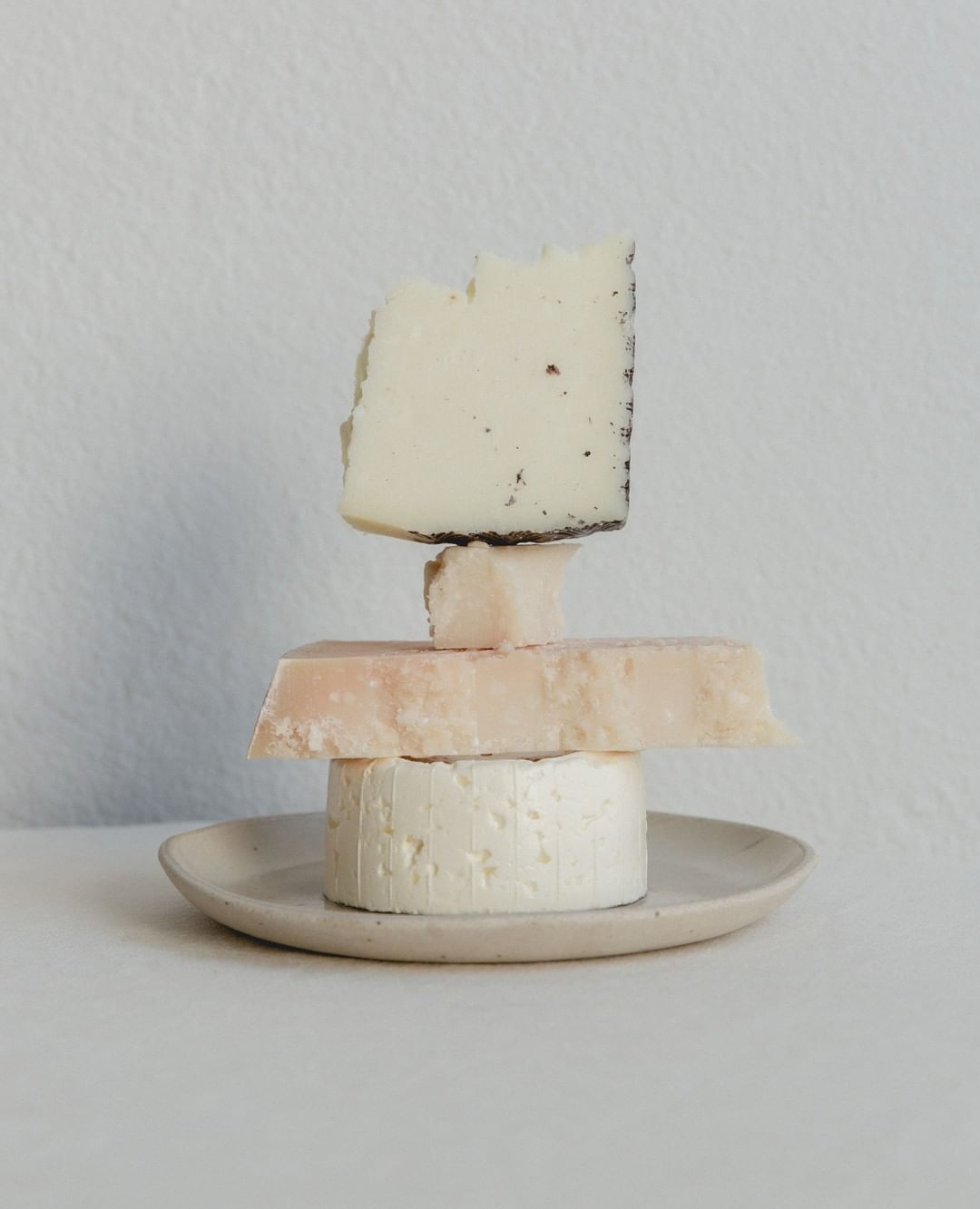 Tower of assorted cheeses on a small plate against a white background. Dairy food photography with neutral tones, studio lighting.