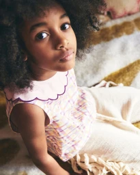 Young child with dark curly hair wearing a pink scalloped-collar top and patterned trousers, photographed from above.
