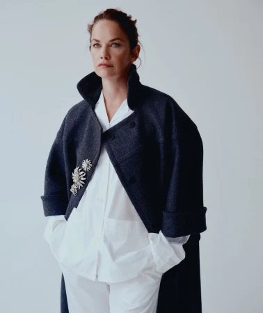 Portrait of a woman wearing a dark oversized coat over a white shirt, photographed by Charlotte Hadden in London.