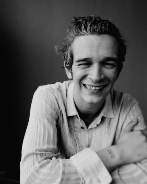 Portrait of a smiling adult male with short, tousled hair, wearing a striped shirt in a black and white indoor shot.