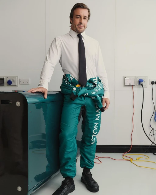 Professional portrait of a male in a semi-formal outfit with a racing jumpsuit over his shoulder, indoors, posing near a teal-colored object.