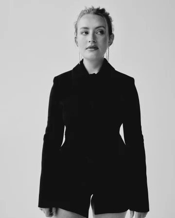 Monochrome portrait of a woman wearing a dark tailored jacket against a plain white background by photographer Charlotte Hadden.