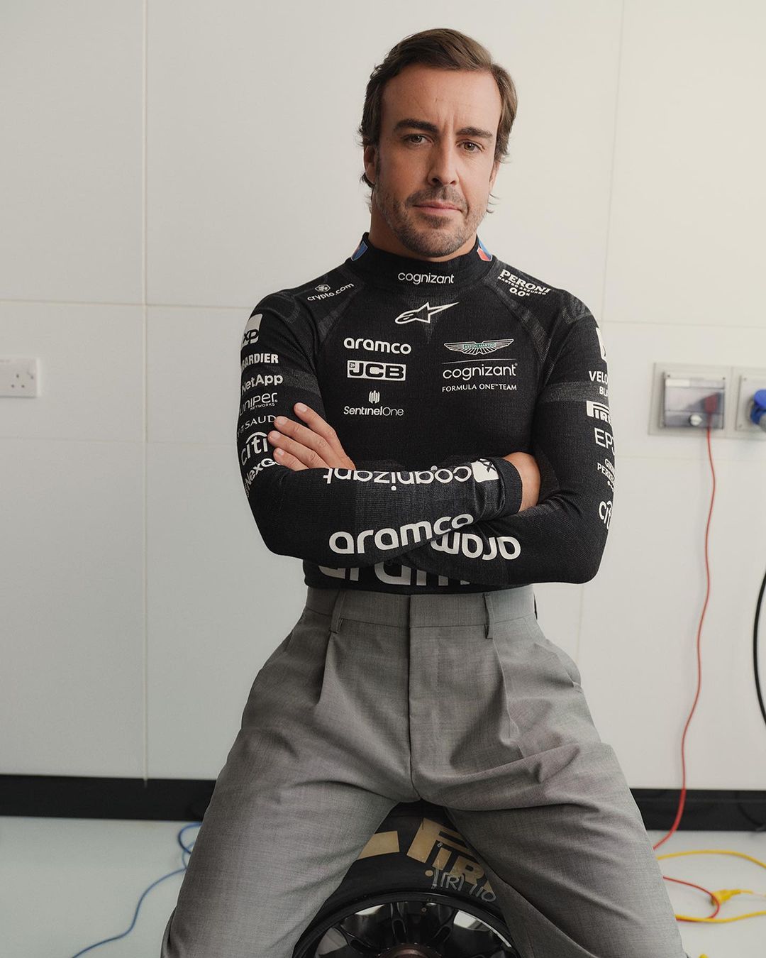 Portrait of Fernando Alonso wearing a black Aston Martin Aramco Cognizant Formula One Team race shirt and gray pants, indoors.