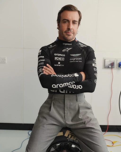 Portrait of Fernando Alonso wearing a black Aston Martin Aramco Cognizant Formula One Team race shirt and gray pants, indoors.