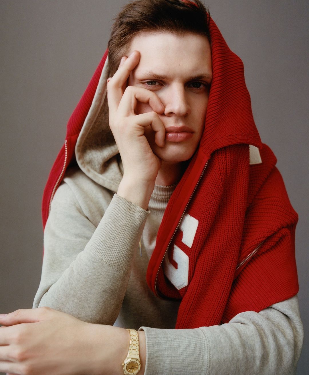 Portrait of a fair-skinned adult male with a red hooded sweater partially draped over his head and shoulders, wearing a gold watch.