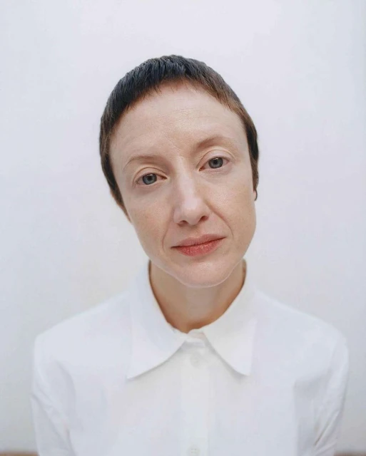 Close-up studio portrait of an adult woman with short brown hair and a white collared shirt against a plain white background.