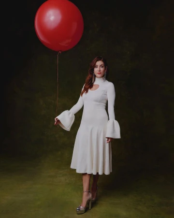 Woman in white dress poses with red balloon against textured background. Fashion shot with elegant dress and platform heels.