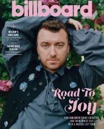 Sam Smith wearing a blue ruffled shirt and black vest amid pink flowers photographed by Charlotte Hadden