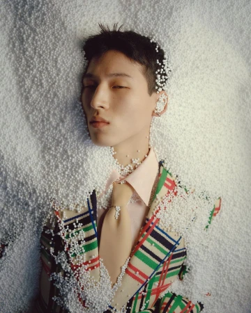 Man wearing patterned blazer and tie surrounded by small white polystyrene beads in studio portrait