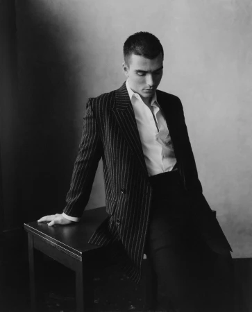 Monochrome portrait of a man in a pinstriped suit jacket and white shirt leaning on a dark table