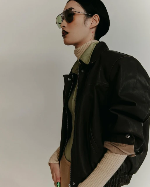 Portrait of an adult woman with dark lipstick, wearing a black beret, aviator sunglasses and a black leather jacket indoors.