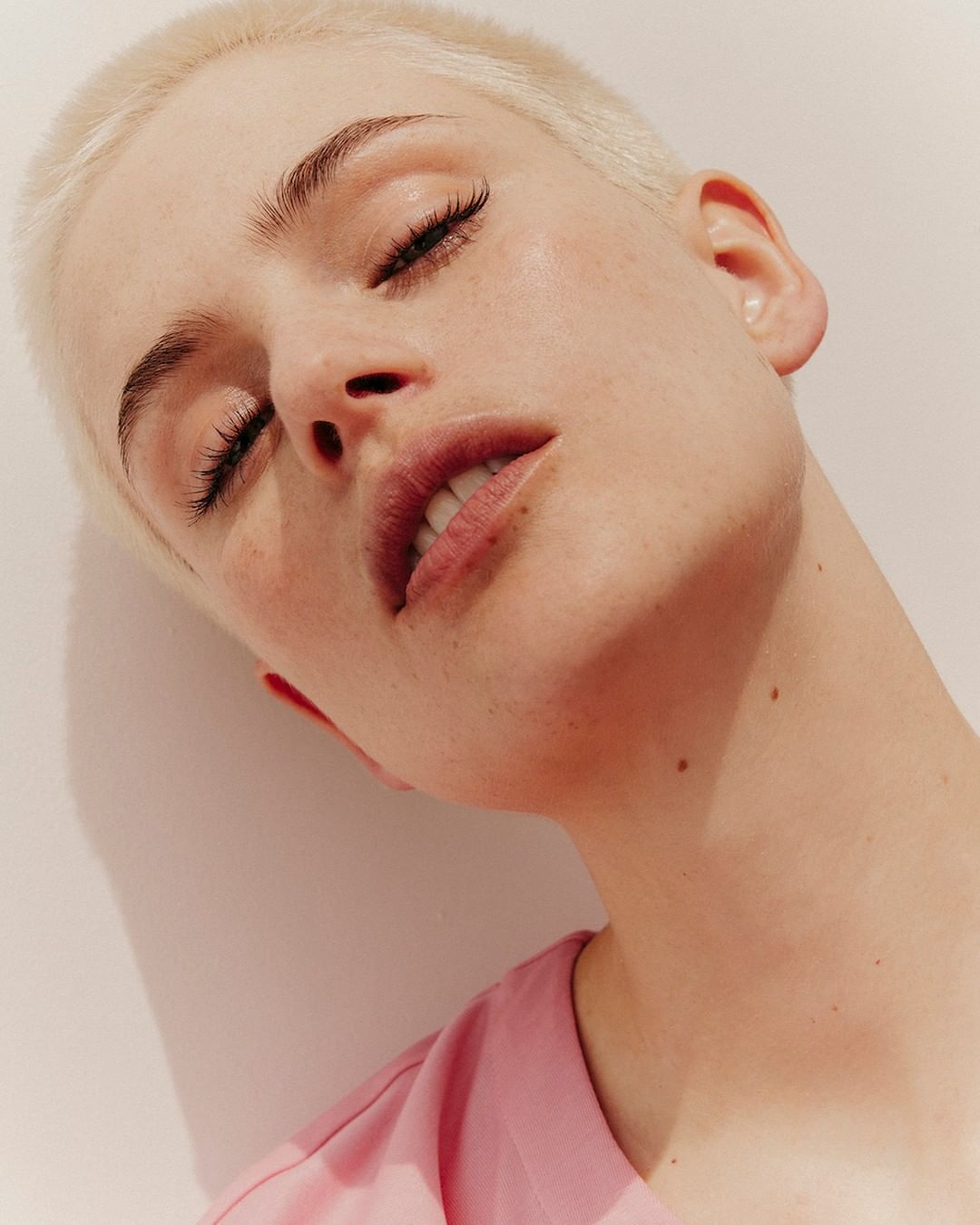 Close-up portrait of a woman with short blonde hair and pink top against a neutral background by Charlotte Navio