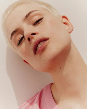 Close-up portrait of a woman with short blonde hair and pink top against a neutral background by Charlotte Navio