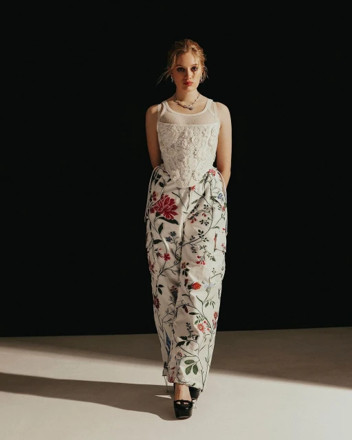 Young woman posing in a fashionable floral-print dress in a studio setting with a dark background and soft, diffused lighting.