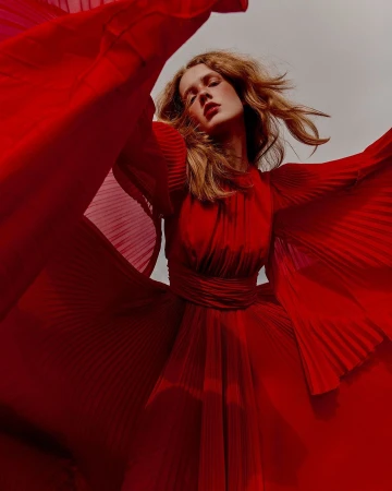 Model in a bright red pleated dress with billowing sleeves posing outdoors against an overcast sky, captured by Charlotte Navio in Paris.