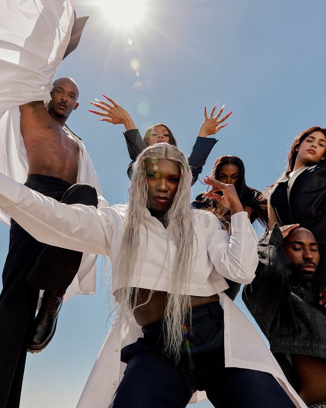 Group portrait of six diverse models in white shirts and black pants against a blue sky with bright sun. Fashion and style.