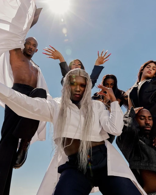 Group portrait of six diverse models in white shirts and black pants against a blue sky with bright sun. Fashion and style.