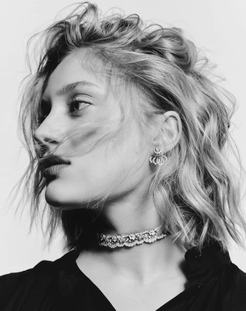 Black and white portrait of a young woman with wavy blonde hair wearing a lace choker and earrings, posing against a plain background.