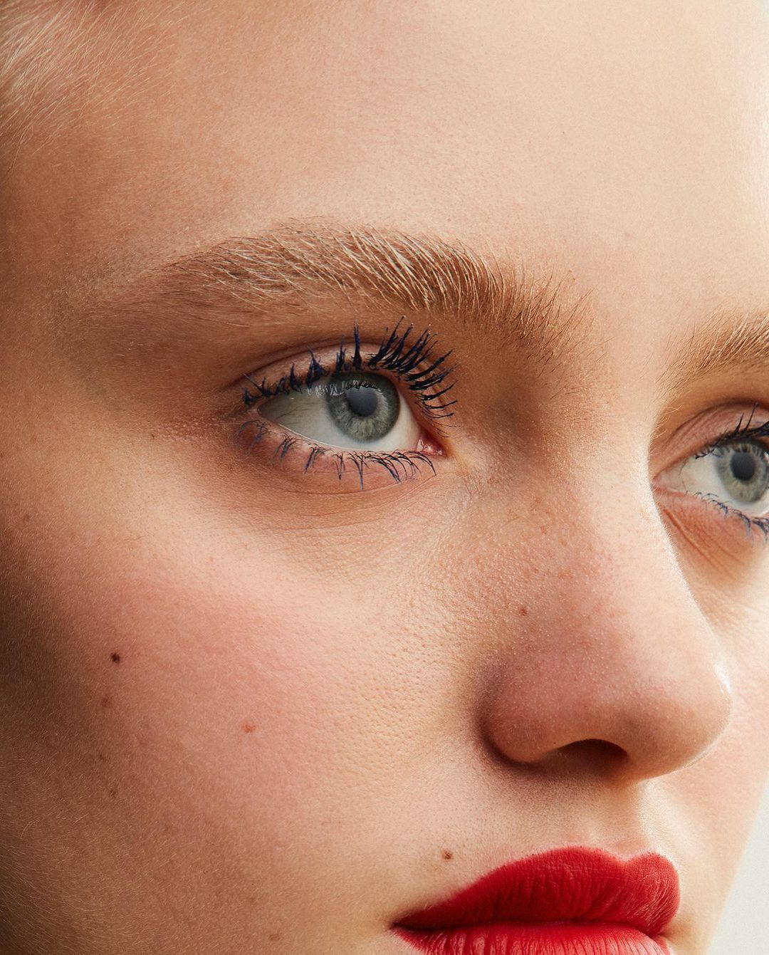 Close-up of a woman's face with fair skin, blue eyes enhanced with mascara, and red lipstick, showcasing beauty and makeup focus.
