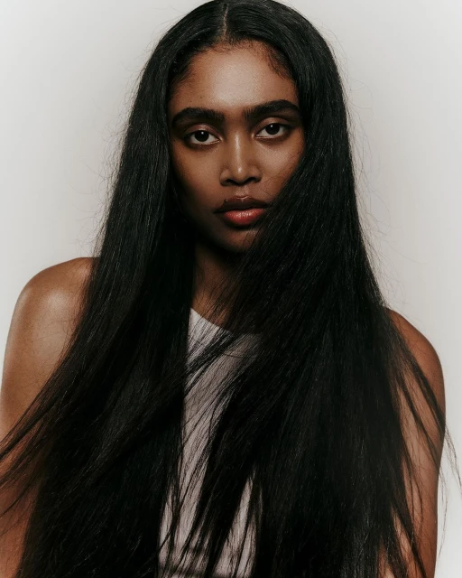 Portrait of a woman with long, straight black hair, medium skin tone, and light-colored tank top against a light grey background.