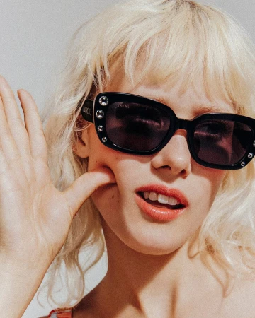 Close-up portrait of a blonde woman wearing black crystal-embellished sunglasses with her hand pressed against her cheek