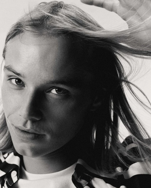 Monochrome portrait of a fair-skinned adult woman with long blonde hair, large hoop earrings, and a spotted shirt, against a white background.