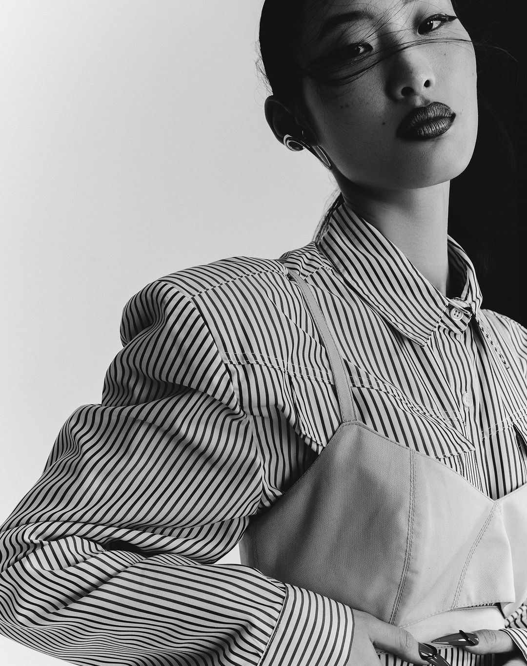 Close-up portrait of an adult woman with fair skin and dark hair styled in a high bun, wearing a striped shirt and dark lipstick.