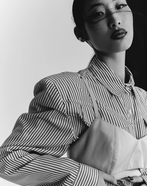Close-up portrait of an adult woman with fair skin and dark hair styled in a high bun, wearing a striped shirt and dark lipstick.