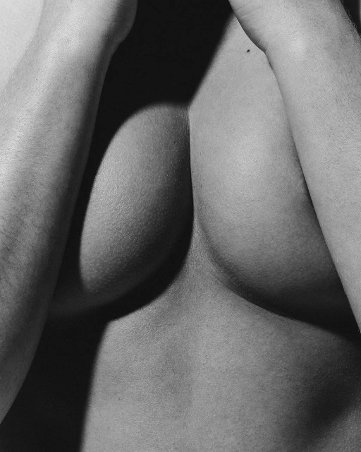 Monochrome close-up of the upper torso of a person with arms raised, creating shadows and highlights on the skin's surface.
