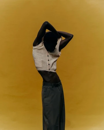 Man wearing a cream sweater vest and dark trousers poses against a warm mustard yellow studio backdrop in Paris